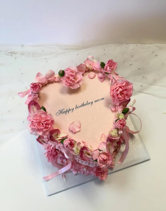 Heart-shaped pink celebration cake adorned with fresh carnations and satin ribbons